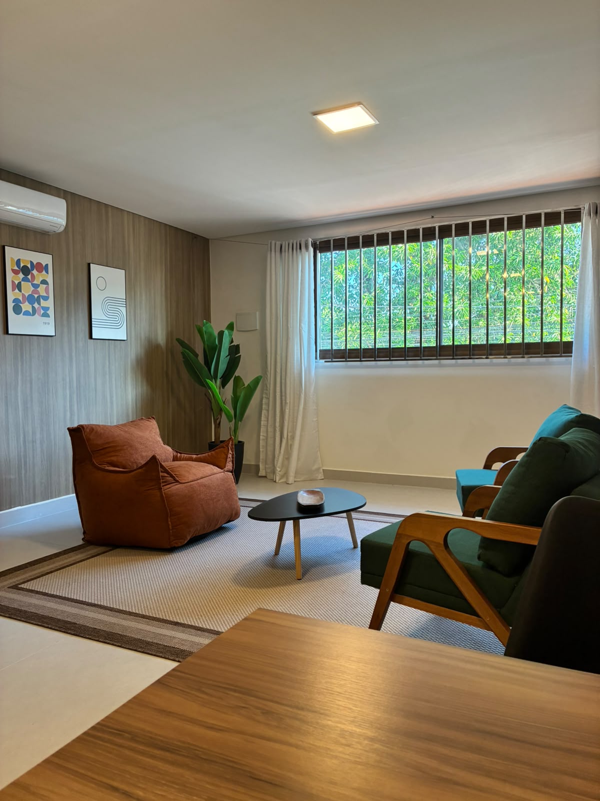 Sala de estar com poltrona terracota, sofás verdes e iluminação natural
